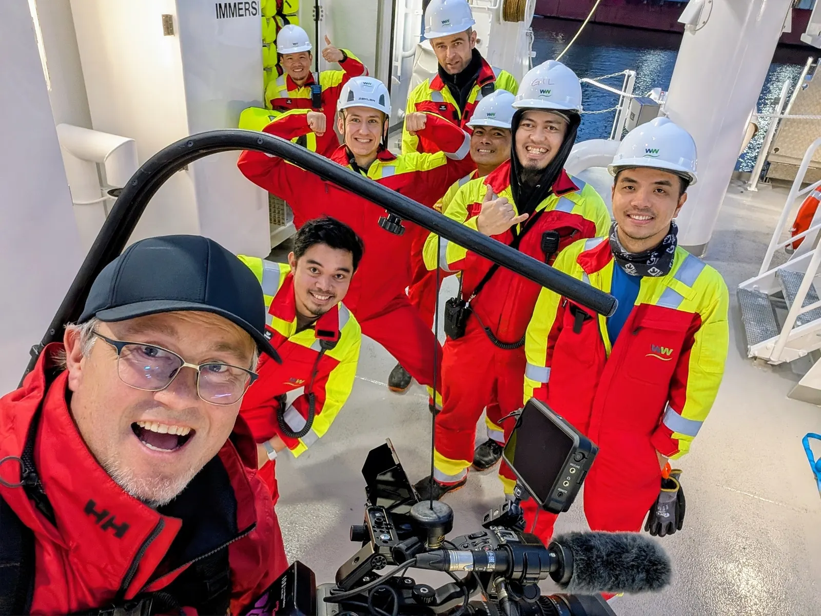 Terje Huse tar selfie med et smilende mannskap i hjelmer og kjeledresser om bord på et skip